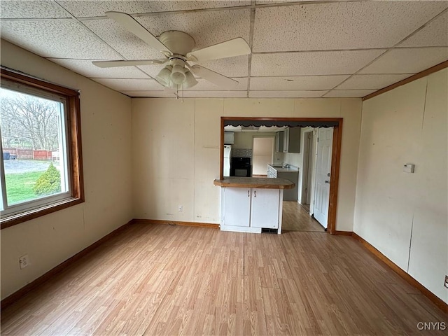 unfurnished living room featuring light wood-type flooring, a paneled ceiling, a ceiling fan, and baseboards