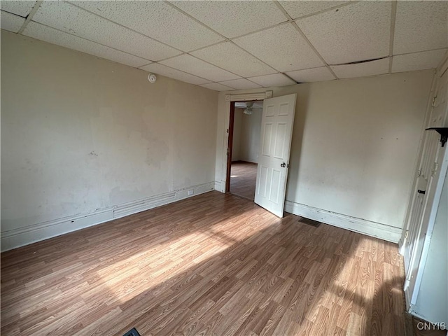 unfurnished room with wood finished floors, a paneled ceiling, visible vents, and baseboards