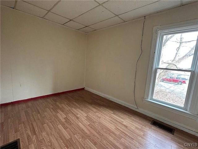 empty room with a paneled ceiling, visible vents, baseboards, and light wood-type flooring