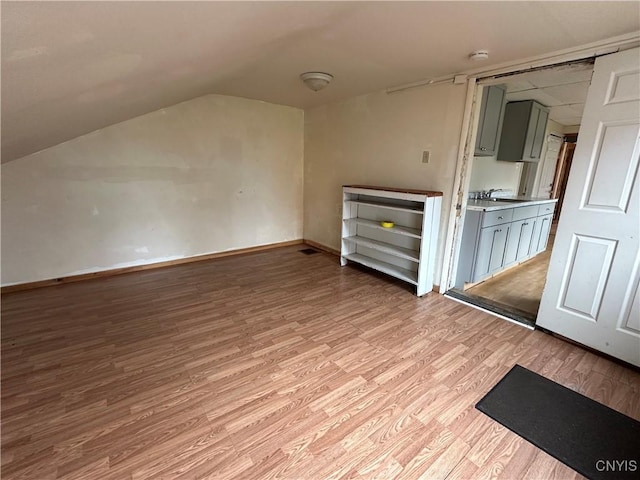 bonus room featuring baseboards, a sink, light wood finished floors, and vaulted ceiling