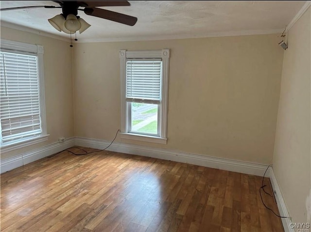 spare room with wood finished floors, crown molding, a ceiling fan, and baseboards