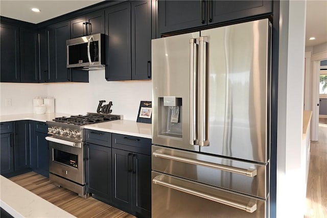 kitchen with recessed lighting, stainless steel appliances, dark cabinets, and light wood finished floors