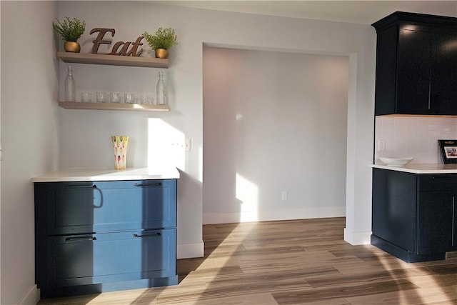 kitchen with wood finished floors, open shelves, light countertops, and dark cabinetry