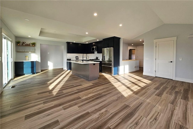 kitchen featuring appliances with stainless steel finishes, light countertops, open floor plan, wood finished floors, and an island with sink