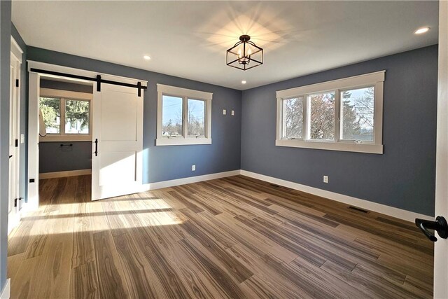 empty room with visible vents, a barn door, baseboards, recessed lighting, and wood finished floors