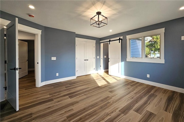 unfurnished bedroom featuring wood finished floors, a barn door, a closet, and baseboards