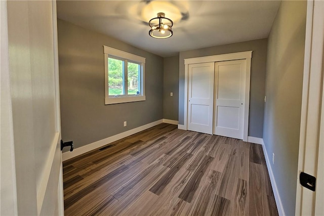 unfurnished bedroom with visible vents, a closet, dark wood finished floors, and baseboards