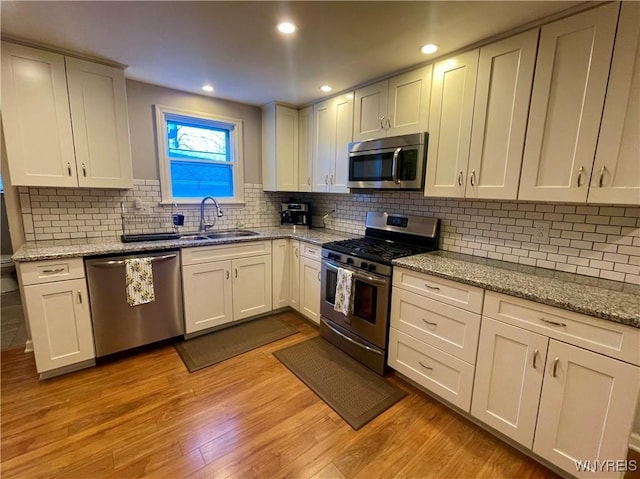 kitchen featuring a sink, light wood-style floors, stainless steel appliances, and decorative backsplash