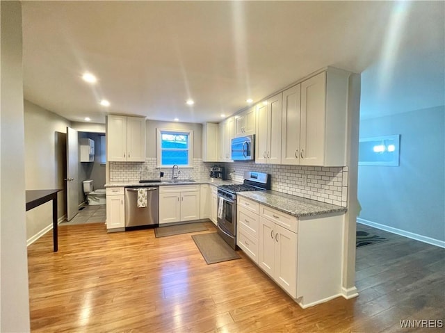 kitchen featuring appliances with stainless steel finishes, backsplash, light wood-style flooring, and a sink