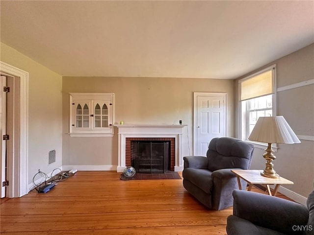 living room with baseboards, visible vents, light wood finished floors, and a brick fireplace