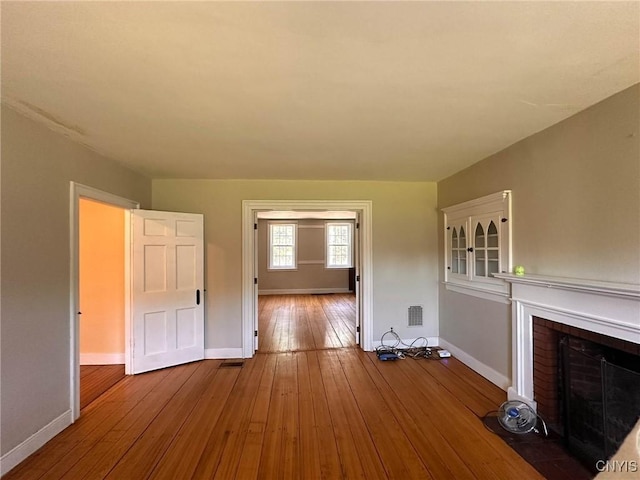 unfurnished living room featuring wood-type flooring, a fireplace, visible vents, and baseboards