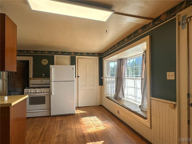kitchen featuring wood finished floors, white appliances, wallpapered walls, wainscoting, and light countertops