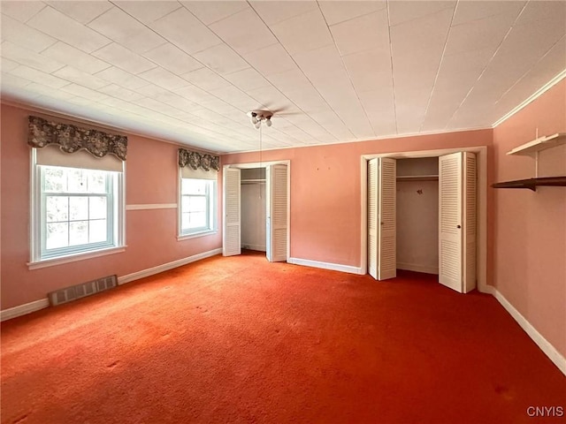 unfurnished bedroom featuring carpet flooring, visible vents, baseboards, ornamental molding, and two closets