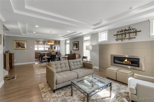 living area featuring recessed lighting, wood finished floors, a fireplace, baseboards, and a tray ceiling