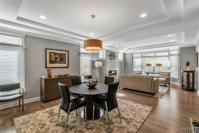dining area with wood finished floors, a raised ceiling, a tiled fireplace, and baseboards