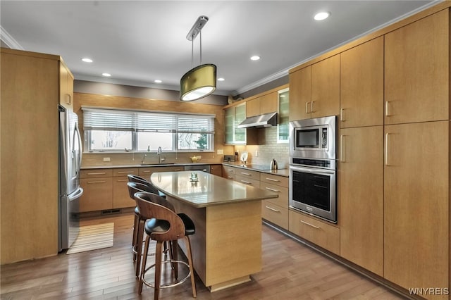 kitchen with a breakfast bar area, under cabinet range hood, appliances with stainless steel finishes, a sink, and crown molding
