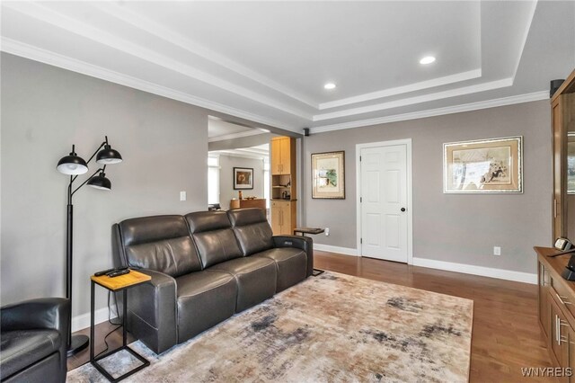 living room with dark wood finished floors, baseboards, ornamental molding, and a tray ceiling