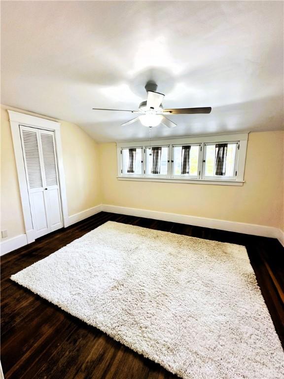 unfurnished bedroom featuring baseboards, multiple windows, a closet, and dark wood-type flooring