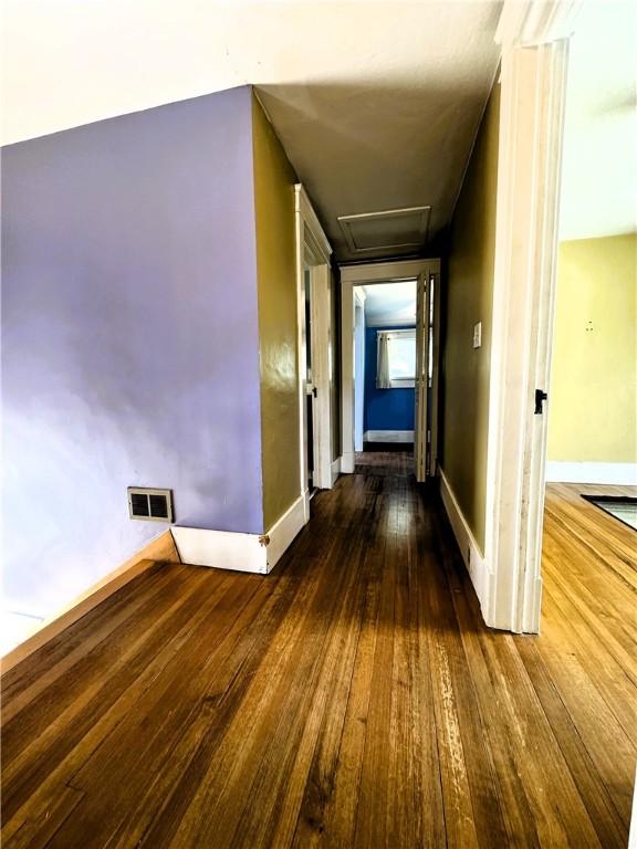corridor featuring baseboards, visible vents, attic access, and wood-type flooring
