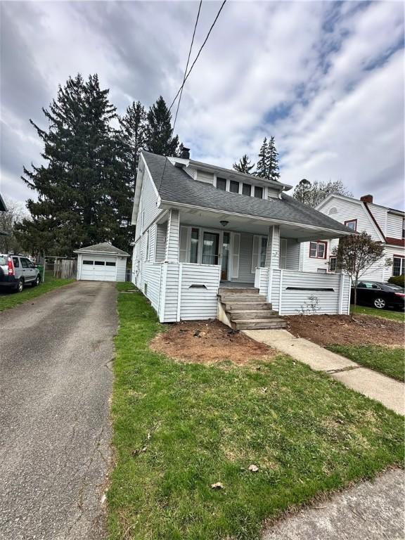 bungalow-style home featuring covered porch, a shingled roof, an outbuilding, a garage, and driveway