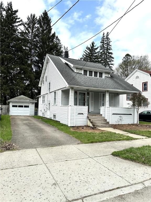 bungalow-style home with roof with shingles, a detached garage, a porch, and an outbuilding