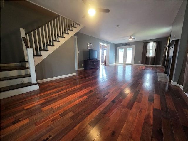 unfurnished living room featuring dark wood-style floors, ceiling fan, stairway, and baseboards