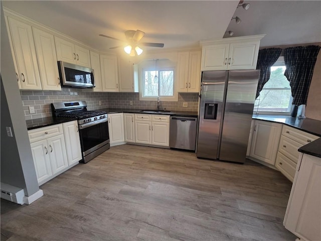 kitchen with a sink, decorative backsplash, dark countertops, appliances with stainless steel finishes, and wood finished floors