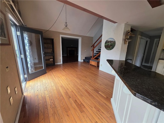 interior space with stairway, light wood-type flooring, vaulted ceiling, and baseboards