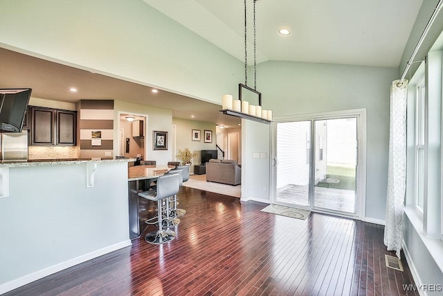kitchen with dark brown cabinetry, a kitchen breakfast bar, high vaulted ceiling, dark wood-type flooring, and light stone counters