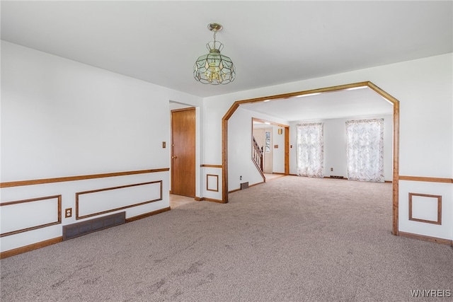 carpeted spare room with arched walkways, visible vents, stairway, and baseboards