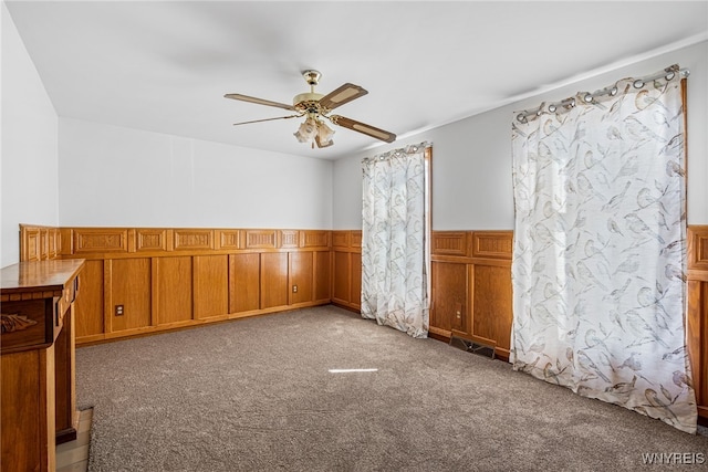carpeted empty room with visible vents, a wainscoted wall, and ceiling fan