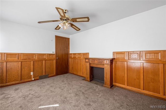 unfurnished living room featuring a wainscoted wall, a ceiling fan, and carpet floors