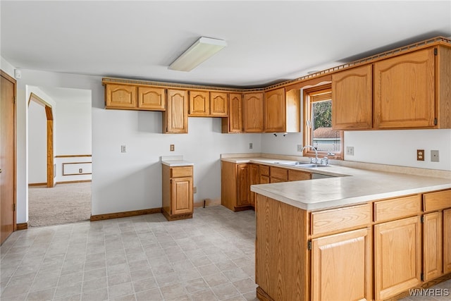 kitchen featuring a sink, a peninsula, brown cabinetry, and light countertops