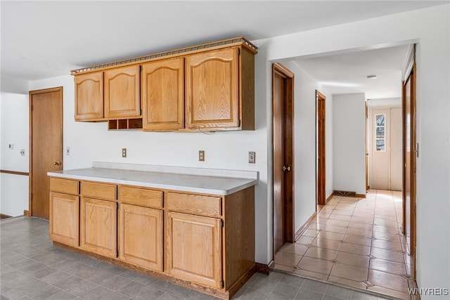 kitchen with light tile patterned floors, light brown cabinetry, baseboards, and light countertops