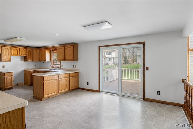 kitchen featuring baseboards, a peninsula, light countertops, and brown cabinets