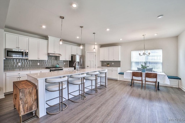 kitchen featuring appliances with stainless steel finishes, a spacious island, light countertops, under cabinet range hood, and a notable chandelier