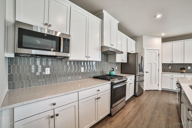 kitchen featuring decorative backsplash, white cabinets, appliances with stainless steel finishes, under cabinet range hood, and dark wood-type flooring