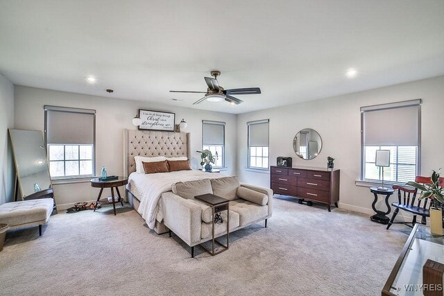 bedroom featuring a ceiling fan, multiple windows, light colored carpet, and baseboards