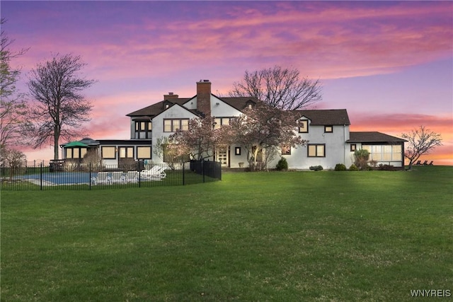 back of house at dusk with a lawn, a chimney, a fenced in pool, and a fenced backyard