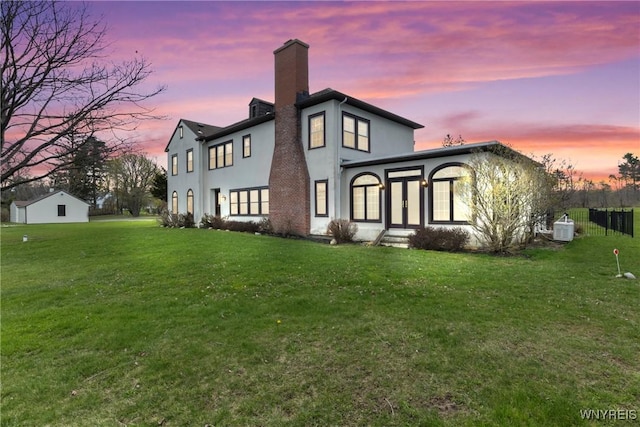 rear view of house featuring a chimney, stucco siding, and a lawn