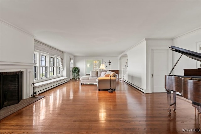 living room with wood finished floors, a baseboard radiator, baseboard heating, ornamental molding, and a fireplace
