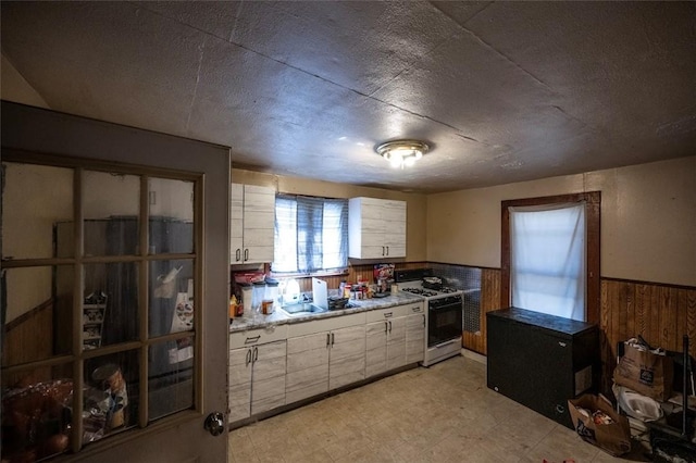 kitchen featuring a sink, white range with gas stovetop, a wainscoted wall, light countertops, and light floors