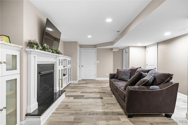 living area with a fireplace with raised hearth, light wood finished floors, recessed lighting, and baseboards