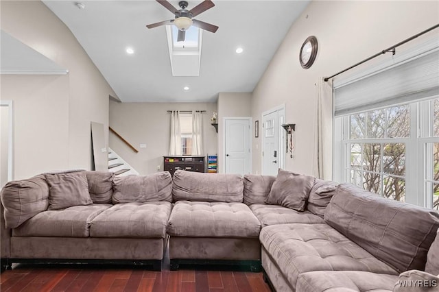 living room featuring stairway, high vaulted ceiling, dark wood-type flooring, a ceiling fan, and a skylight