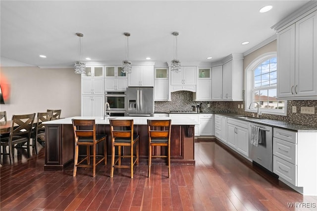 kitchen featuring a sink, glass insert cabinets, a kitchen breakfast bar, a center island with sink, and appliances with stainless steel finishes