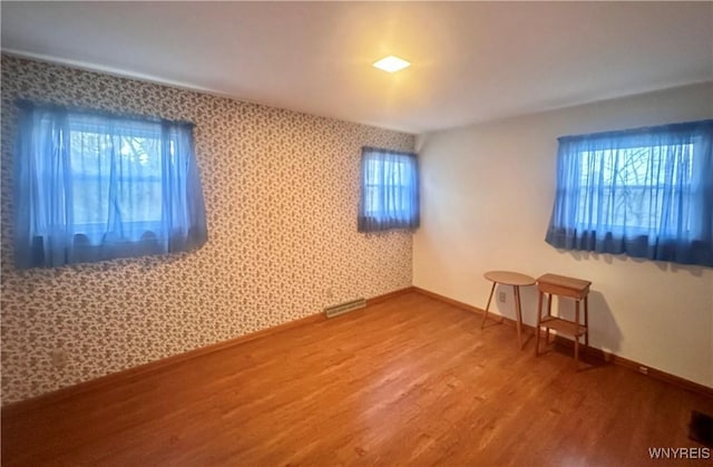 unfurnished room with wood finished floors, visible vents, wallpapered walls, and baseboards