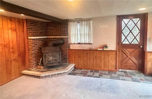 unfurnished living room featuring a wood stove, carpet flooring, and wood walls