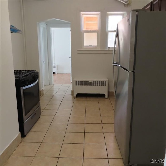 kitchen featuring radiator, arched walkways, light tile patterned floors, and stainless steel appliances