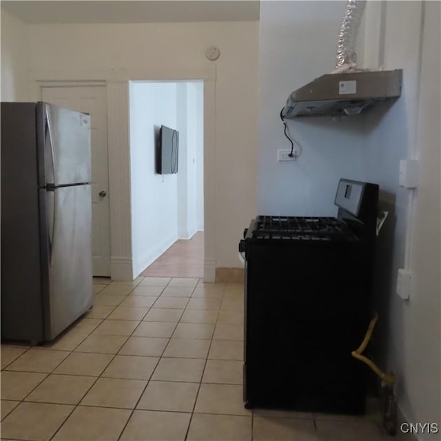 kitchen featuring exhaust hood, freestanding refrigerator, light tile patterned floors, baseboards, and black gas range