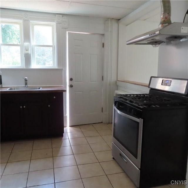 kitchen featuring light tile patterned floors, under cabinet range hood, light countertops, a sink, and stainless steel gas range